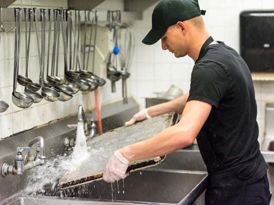 A man washing dishes in a commercial kitchen.