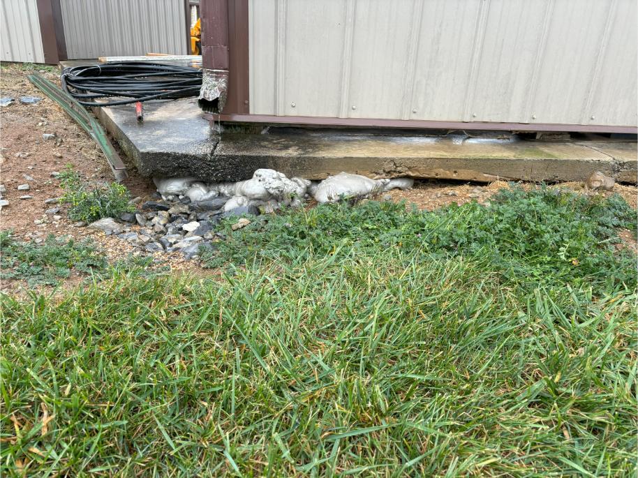 A sunken concrete slab repaired with polyjacking foam. The concrete was lifted to meet the edge of the shed.
